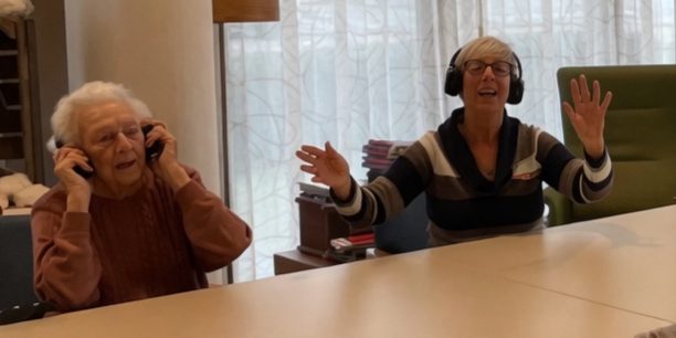 Two residents with headphones at the table, one of them waving along to the music