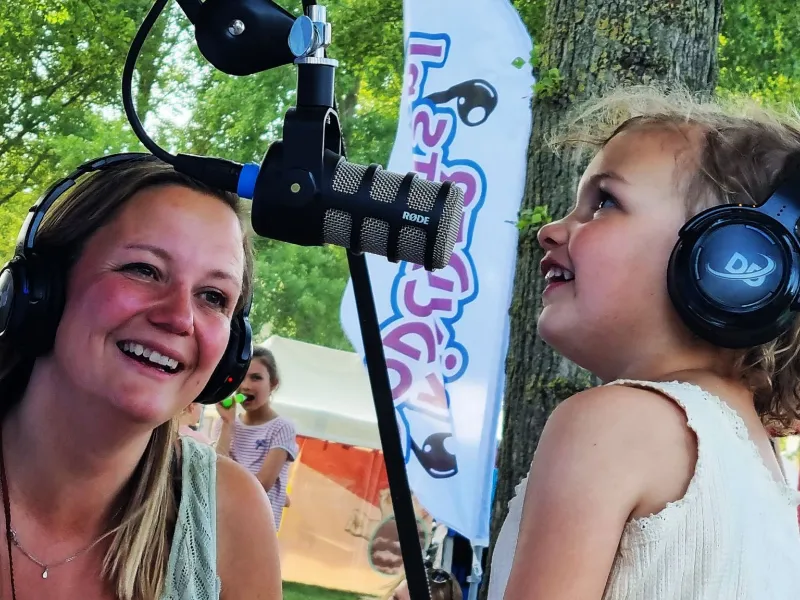 Žena a dievča so slúchadlami pri podcastovom stánku na festivale